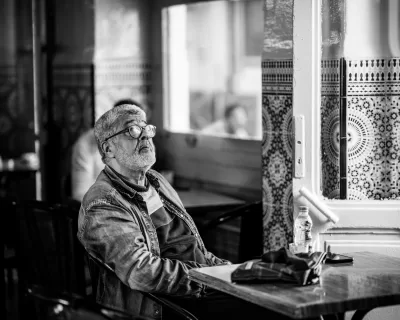 DSCF5916 Candid black and white street photo of man sat at a table in cafe alone watching apparent tv